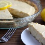 Lemon pie with one slice ona plate, a fork and a lemon off to the side