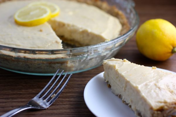 Lemon pie with one slice ona plate, a fork and a lemon off to the side