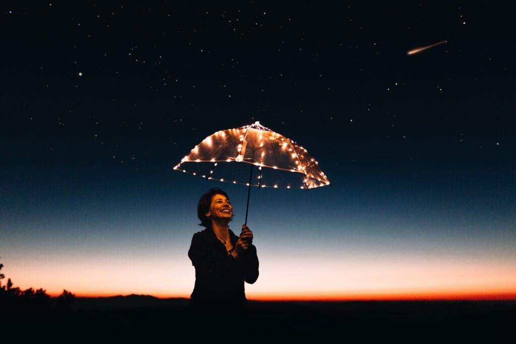 Smiling woman on a starry night holding an upbrella with lights on it