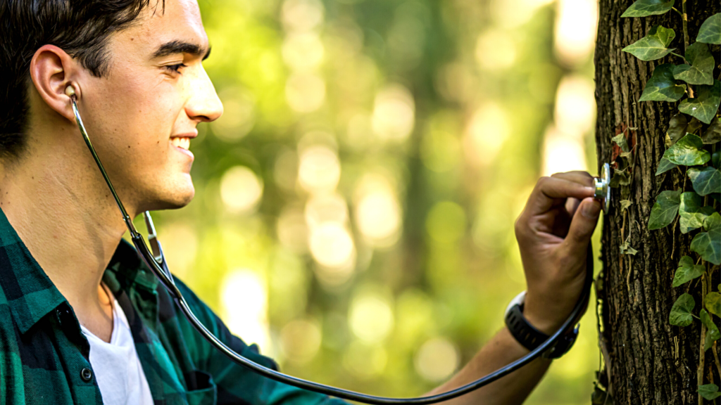 Young man holding a stethoscope on a tree trunk 