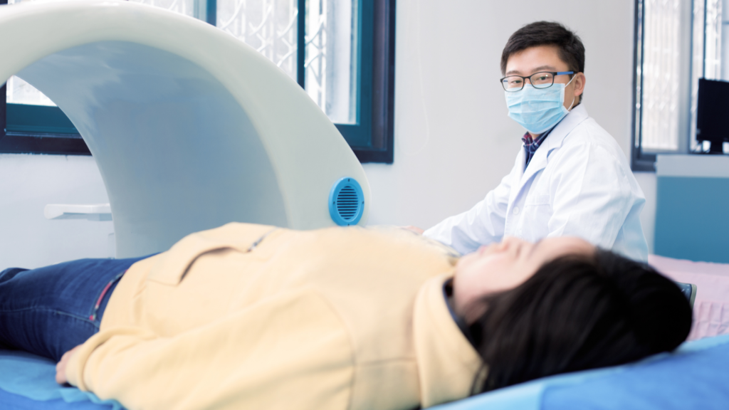 Woman lying in DEXA scan machine, tech with face mask in background