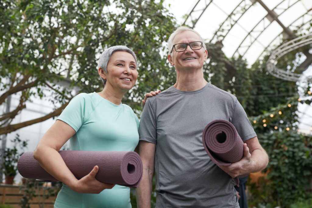 Smiling middle aged man and woman holding yoga mats