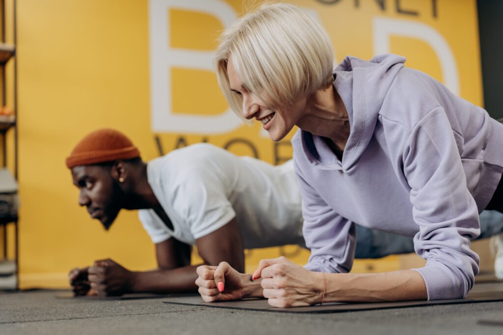 Middle aged beautiful blond woman and attractive black man doing forearm planks